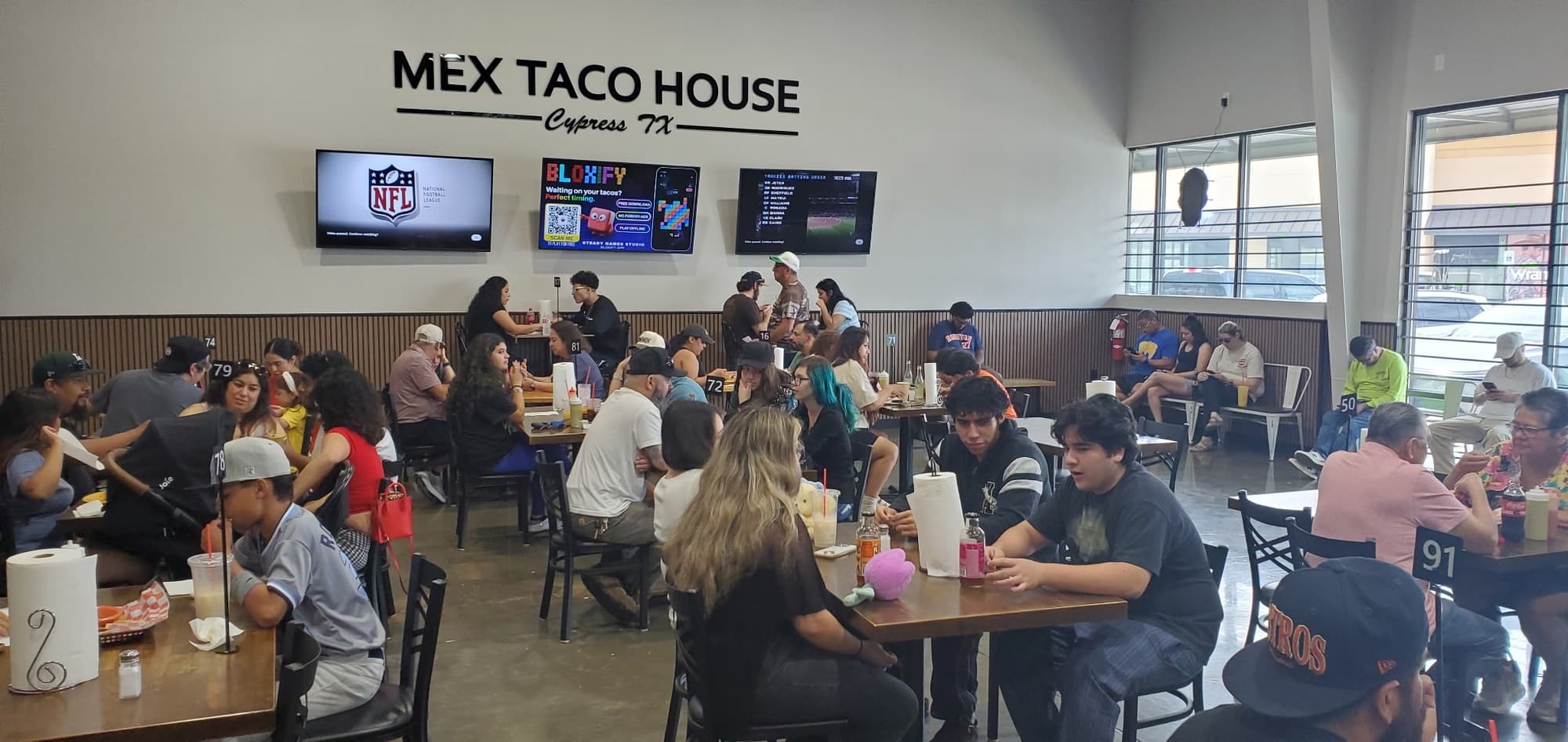 A full dining room at Mex Taco House in Cypress, TX, with a client's ad playing on the wall screens